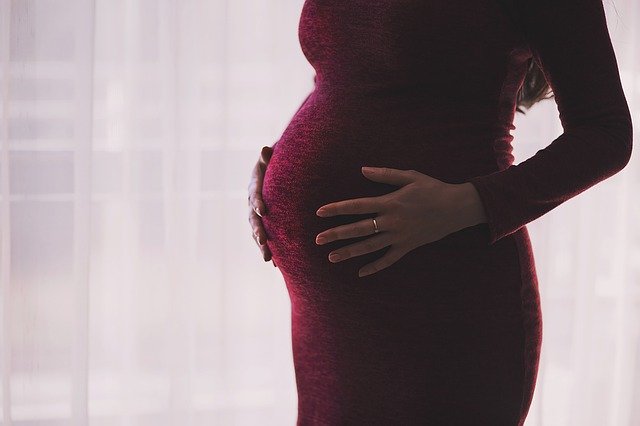 Mensagem de Deus Para as Mães - Imagem de Mulher grávida com as mãos na barriga vestida com uma blusa de manga roxa