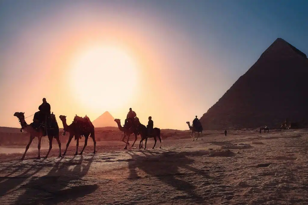 JosÃ©: five persons riding camels walking on sand beside Pyramid of Egypt