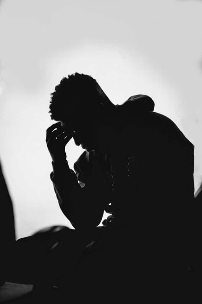 Por que Deus permite o sofrimento: man in black hoodie covering his face with his hands