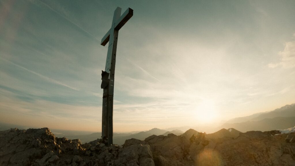A cross on top of a mountain with the sun in the background
